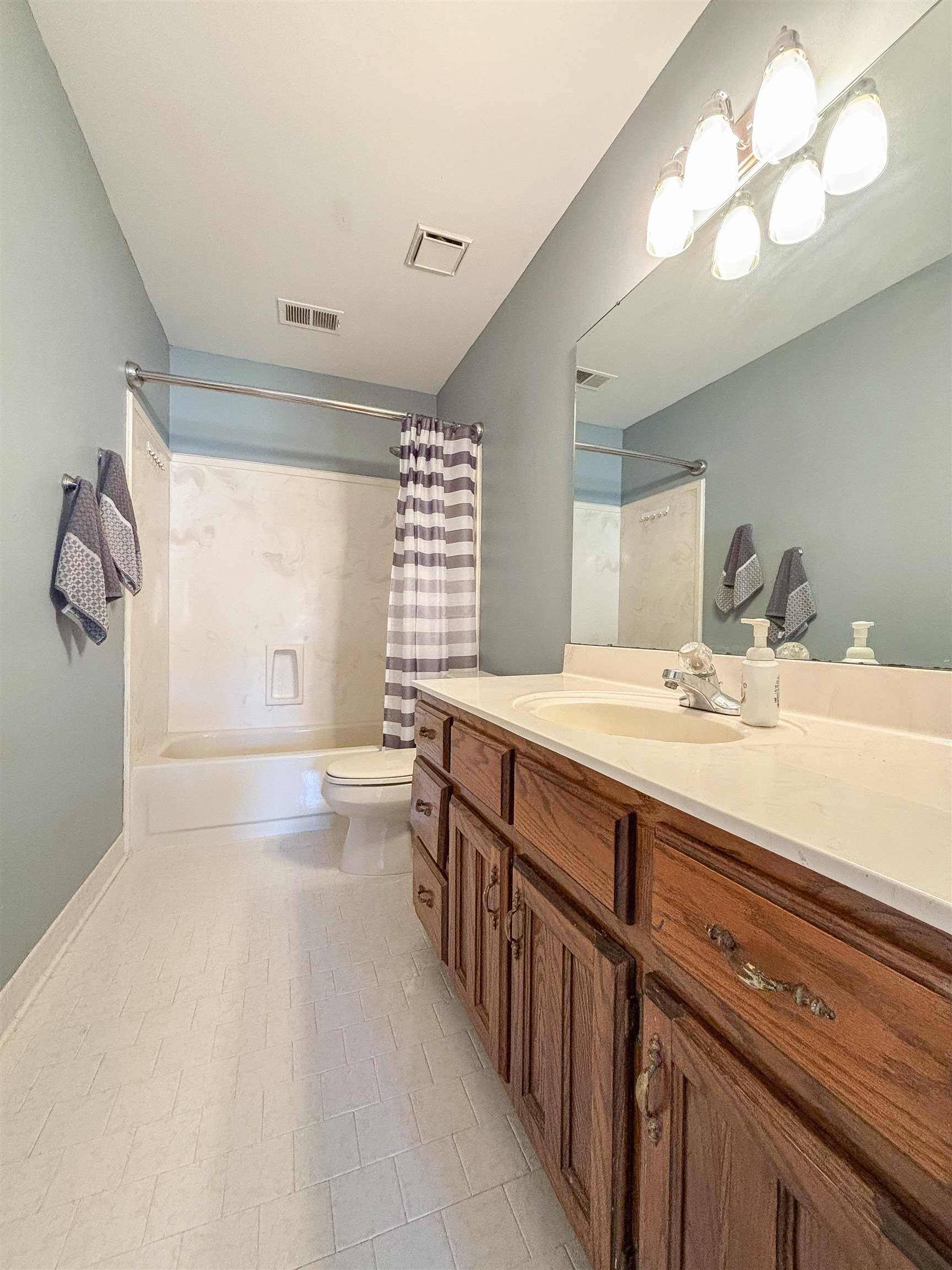 Full bathroom with tile patterned floors, shower / bathtub combination with curtain, vanity, and toilet