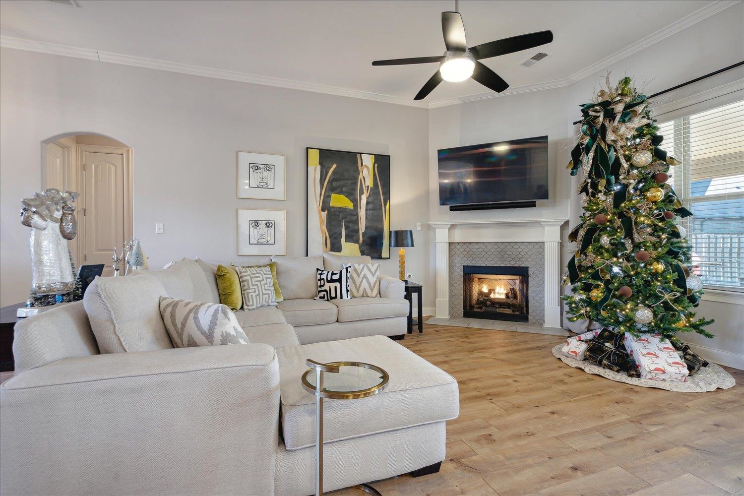 Living room with ceiling fan, a fireplace, wood-type flooring, and ornamental molding