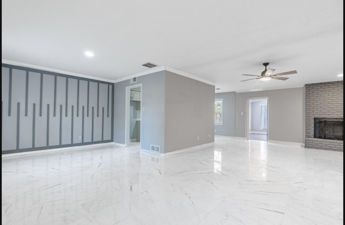 Unfurnished living room featuring crown molding, ceiling fan, and a brick fireplace