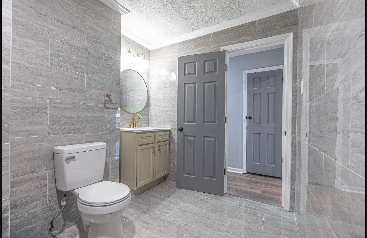 Bathroom featuring a textured ceiling, vanity, toilet, and tile walls