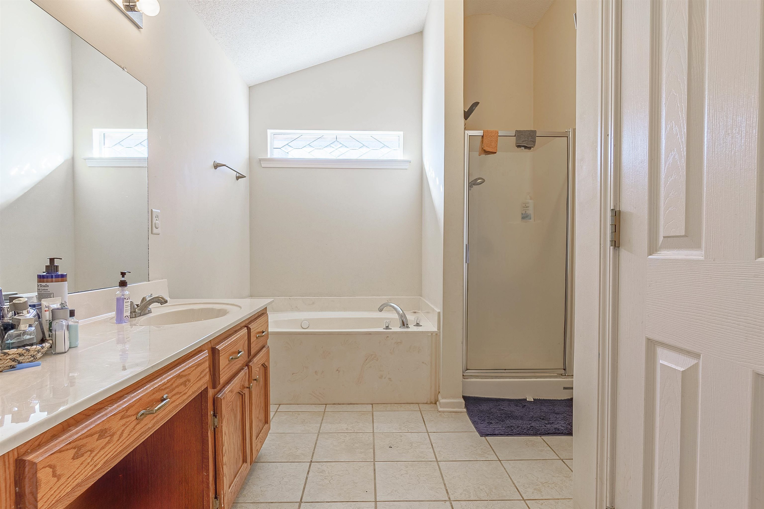 Bathroom with tile patterned floors, a textured ceiling, vanity, separate shower and tub, and lofted ceiling