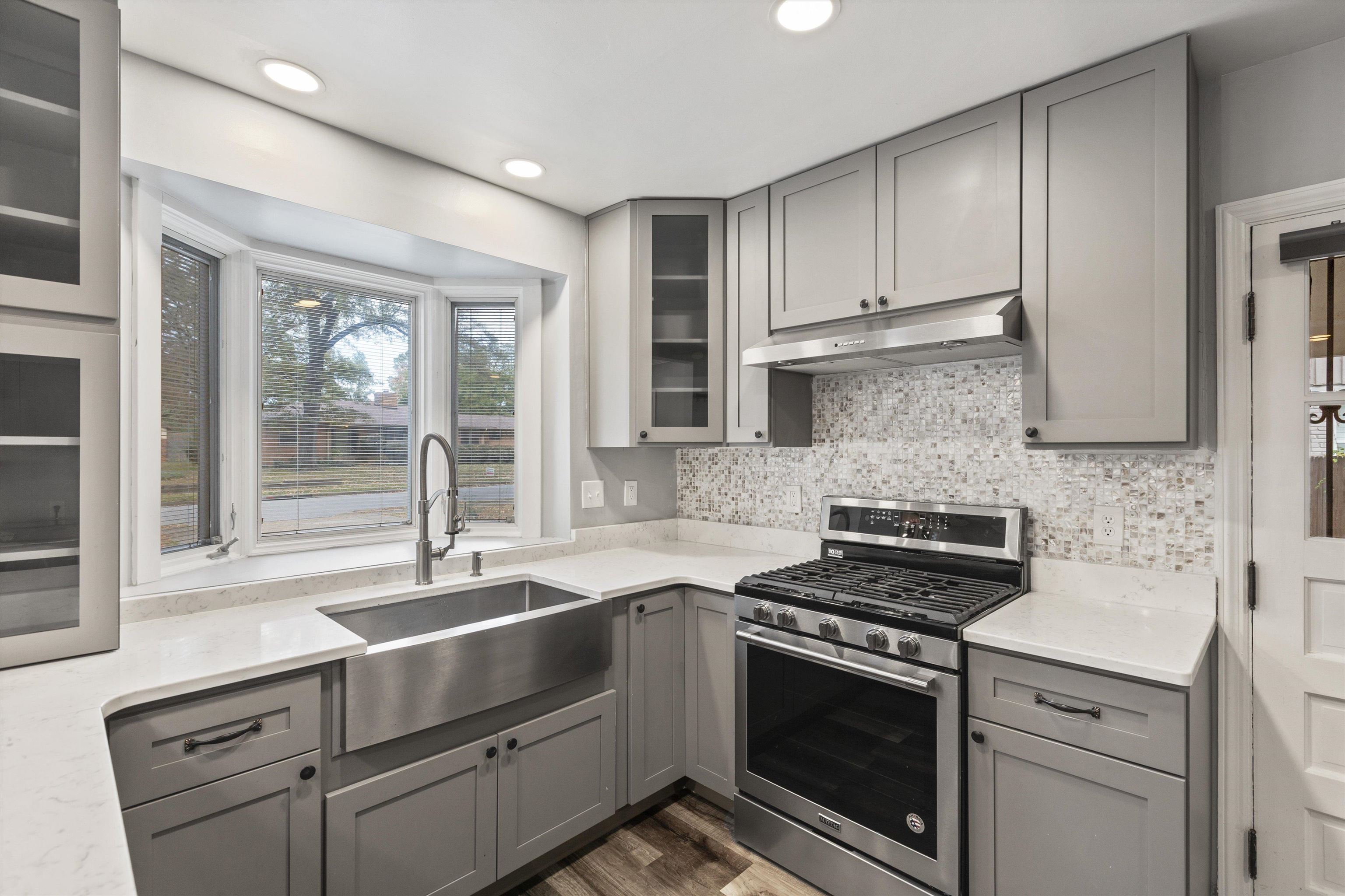 Kitchen featuring decorative backsplash, gas stove, dark wood-type flooring, sink, and gray cabinets