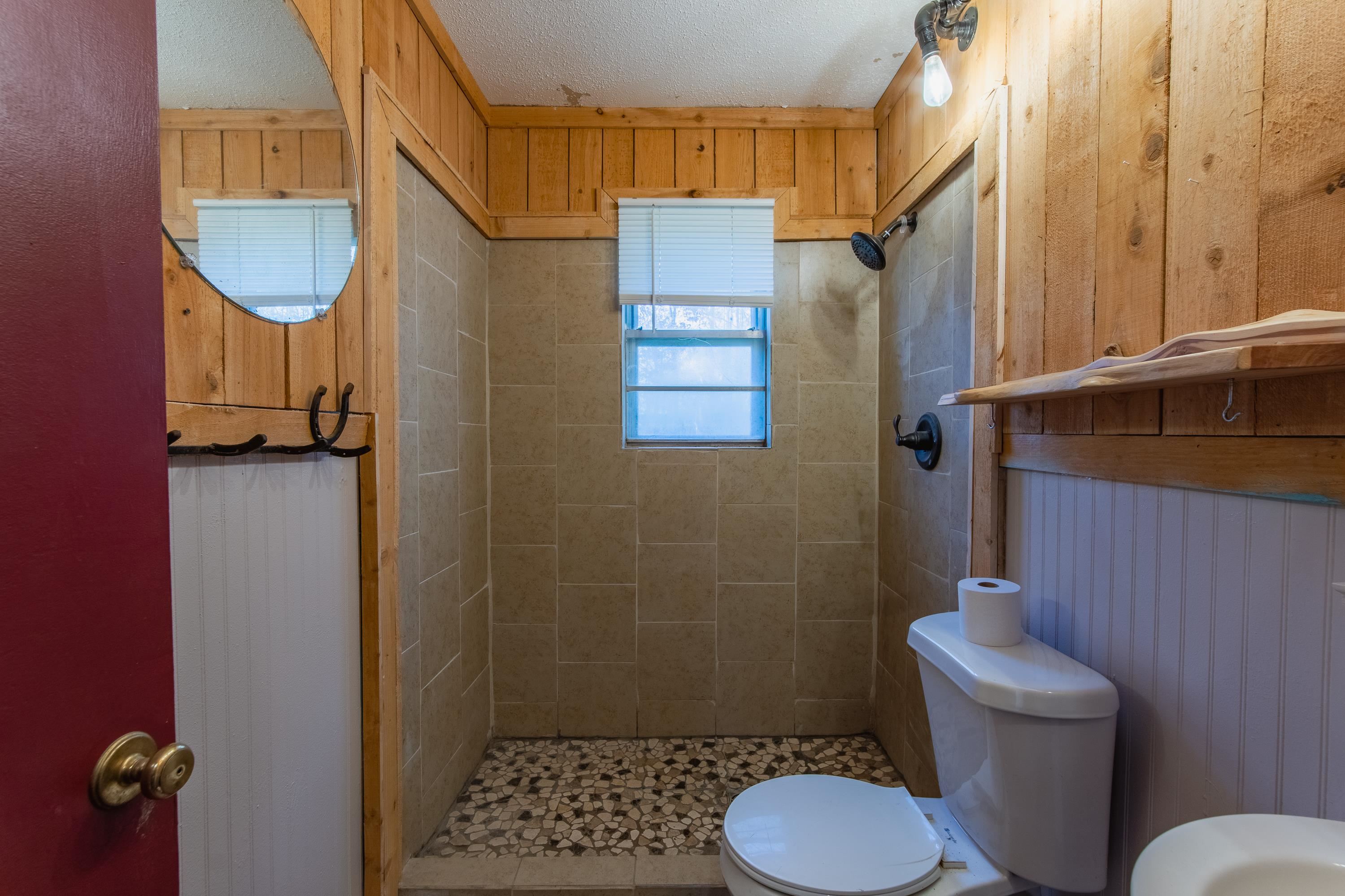 Bathroom featuring wood walls, tile patterned floors, toilet, a textured ceiling, and a tile shower