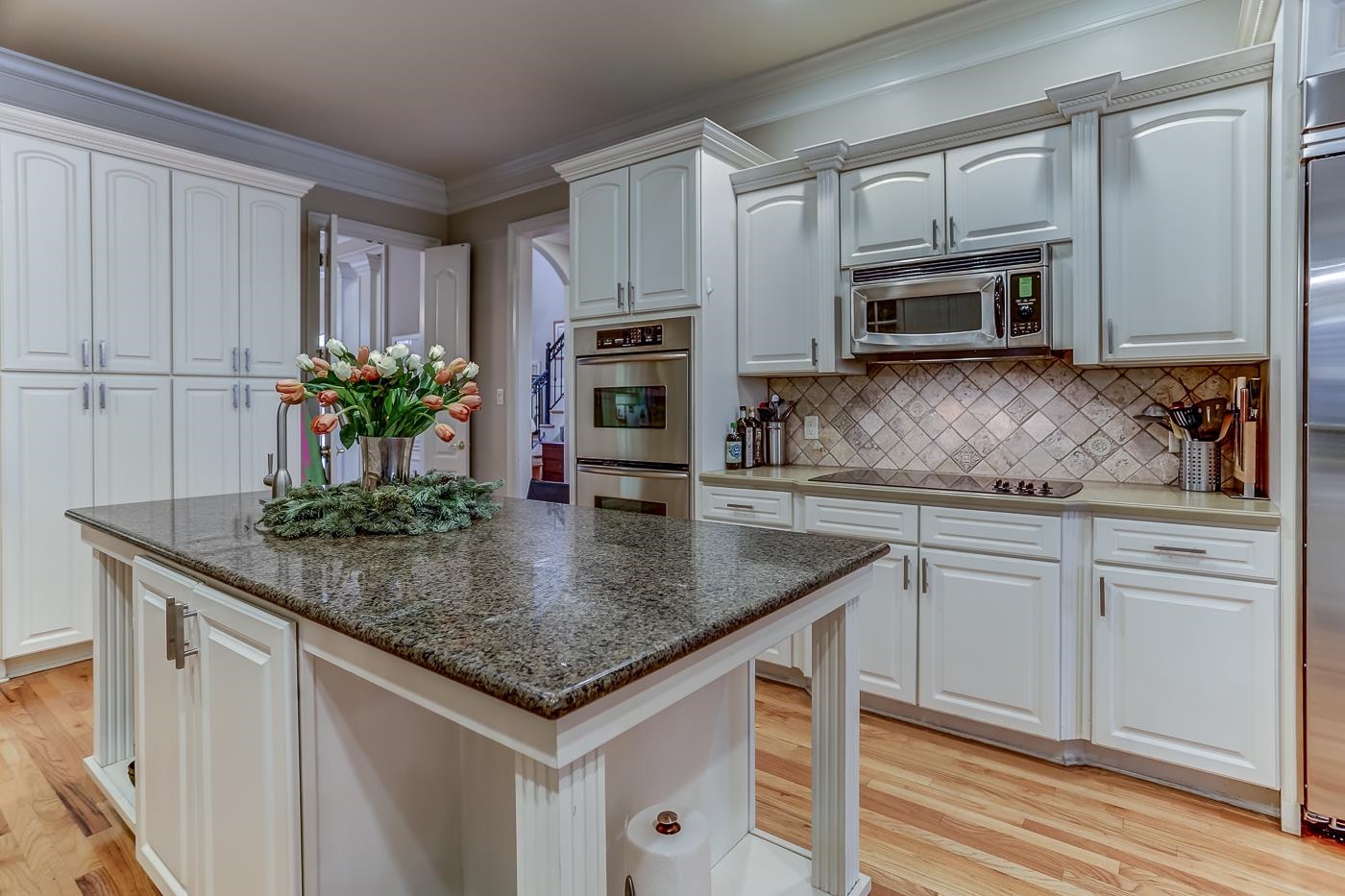 Kitchen with white cabinetry, stainless steel appliances, light wood-type flooring, a kitchen island, and ornamental molding