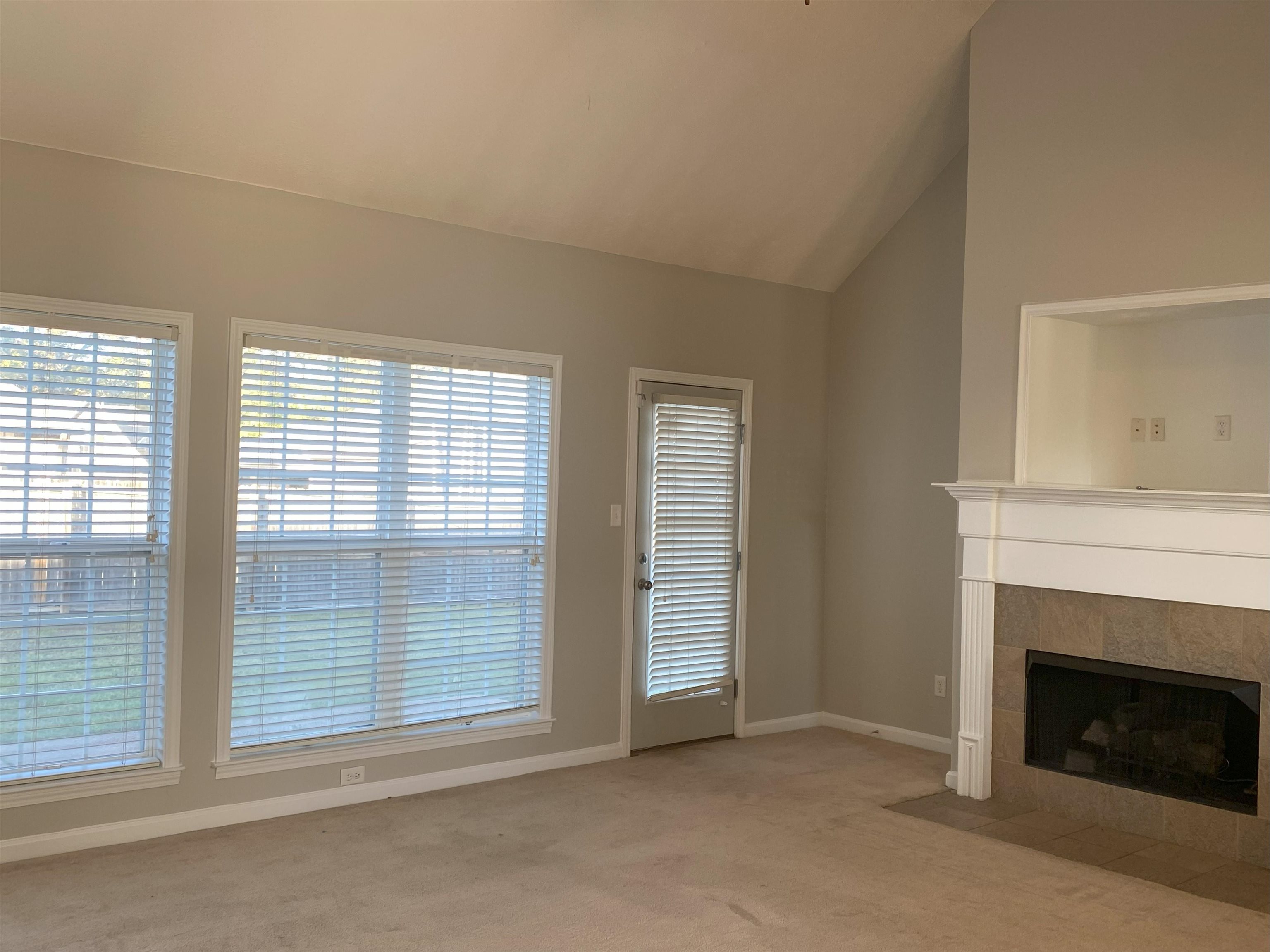 Unfurnished living room featuring a tile fireplace, light carpet, and vaulted ceiling