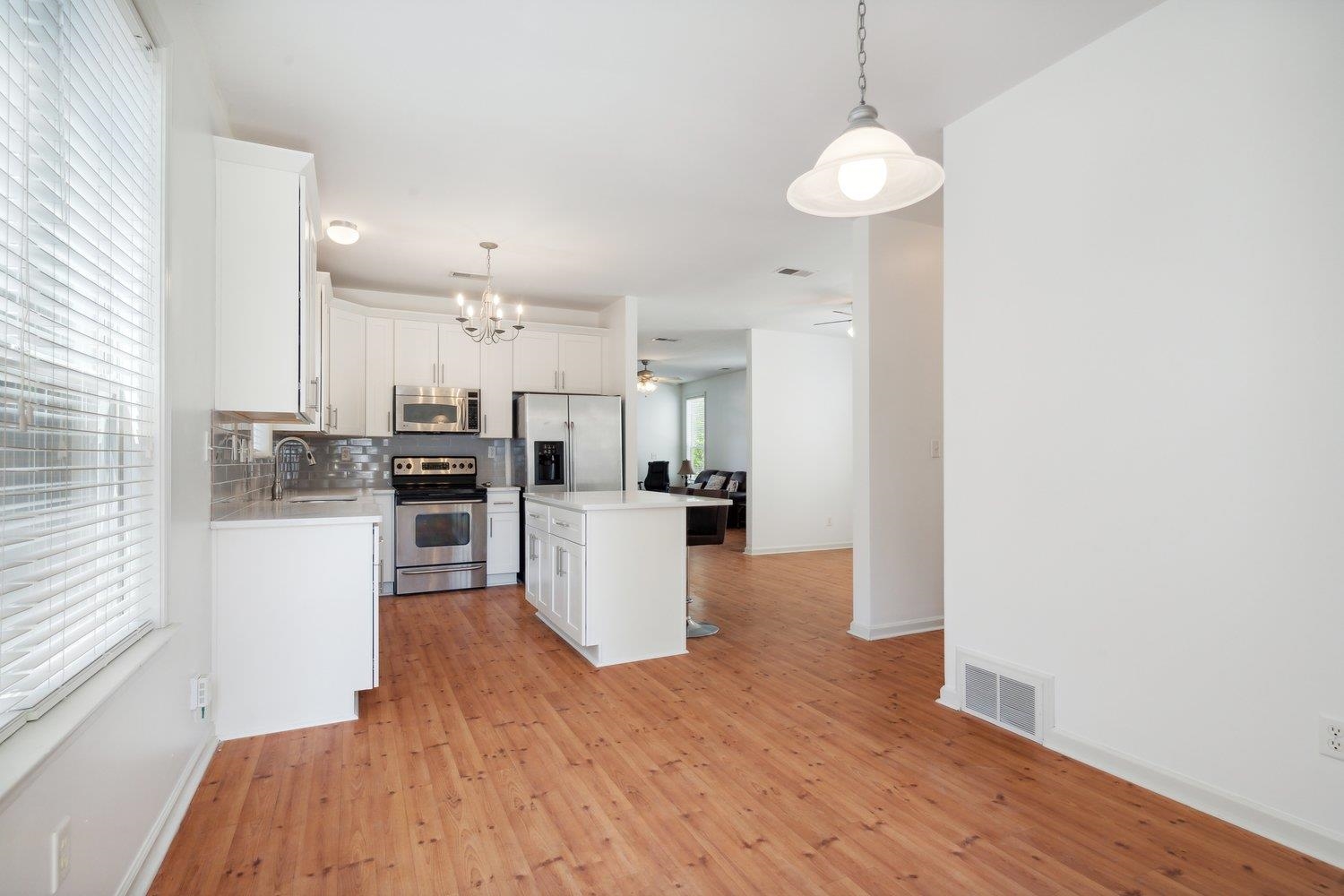 Kitchen featuring light hardwood / wood-style flooring, a kitchen island, stainless steel appliances, hanging light fixtures, and white cabinetry