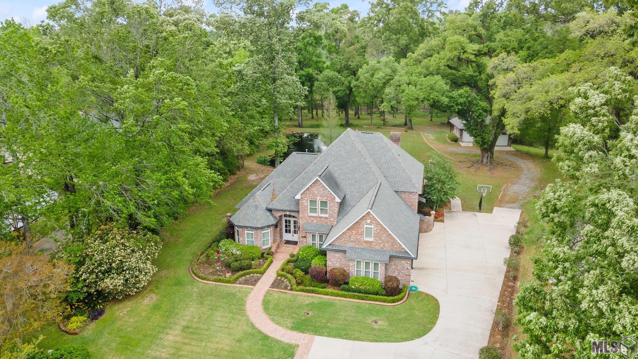 Welcome home to custom, serene estate in the middle of the city. This 1 owner home sits on 2.87 picturesque acres. The back of the property sits on Bayou Manchac at the back of The Country Club of Louisiana. Some of the property's many features include: a whole home generator, pond, outdoor fireplace, 732sqft shop with bathroom & porch, storage area behind shop, partially wooded in rear, Bayou Manchac, ample parking, and 1,600sqft of concrete (covered and not covered) outdoor entertaining area! Upon entering the home, one cannot help but notice the 12ft foyer ceiling. The home first floor of the home is sure to wow! The first floor features Open living and dining areas for entertaining while featuring a triple split floor plan for privacy at every turn! The first floor also features a guest bedroom with attached bath, wet bar, mud room, sprawling laundry room, private study with wood barn doors, half bath for guest, built-in entertainment case, floor to ceiling windows, central home vacuum system, AMPLE storage, DUAL bathrooms in the primary suite and so much more! Upstairs features two bedrooms, 1.5 bathrooms, a game room, and bonus room with a closet! A true must see! Call today to schedule your private showing of this one of a kind property!