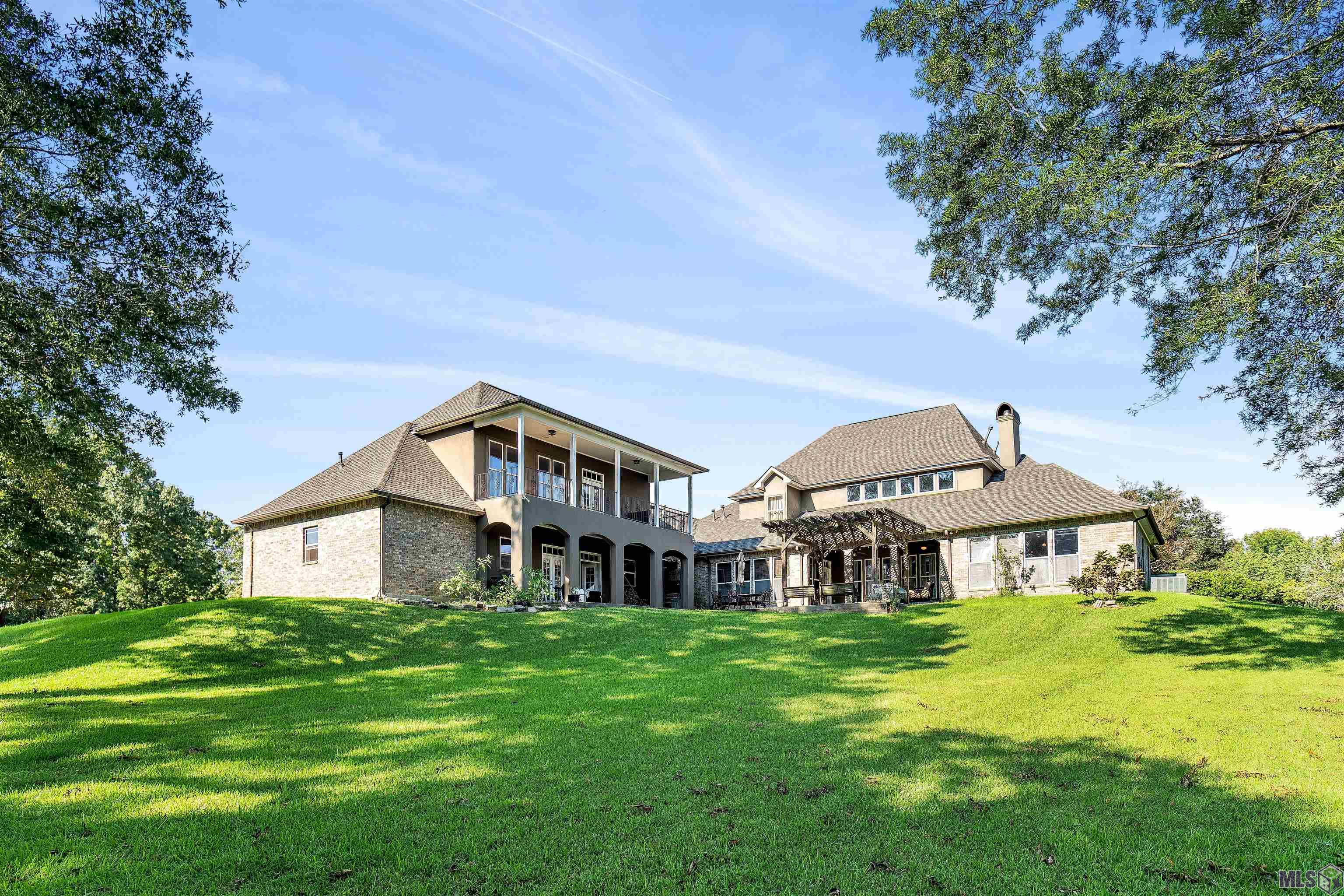 [Pre-Inspection Included] Imagine hosting a grand wedding reception or a cozy Christmas dinner at this 5-bedroom, 5-bath custom home nestled on nearly an acre in the prestigious Manchac Plantation, part of the highly sought-after Ascension Parish school district. Designed with entertainment in mind, this home is a stage for life’s memorable moments. As you step through the grand foyer, adorned with Corinthian columns, you're greeted by the warm glow of heart of pine wood floors and triple crown molding, setting the tone for a residence rich in detail and design. The heart of the home is a chef’s kitchen featuring custom cypress cabinets, an expansive island, and a high-end Thermador range with all the bells and whistles—including four burners, two griddles, and a pot filler. This kitchen isn’t just for cooking; it serves as a central gathering spot, open to sitting areas and the dining room, perfect for entertaining or enjoying morning coffee while overlooking the yard with its mature oak.The living room, with soaring ceilings and a wall of windows, fills the space with natural light and is anchored by a stylish gas fireplace with marble surround. The main floor hosts two bedrooms—the primary suite offers luxury and comfort with its own fireplace, sitting area, and a lavish en suite bath with a soaking tub, custom shower, and dual vanities. Another bedroom, also on the main floor, includes a full bath and walk-in closet. Upstairs, discover three additional bedrooms and two full baths. Up another flight of stairs, a secluded game room awaits. This bonus space, over the garage, boasts its own bath, bar, and private balcony—perfect for entertainment. Outside, nearly an acre of fenced grounds includes two covered porches and a patio area, all surrounded by picturesque oak trees—ideal for outdoor gatherings. Minutes from Baton Rouge, with access to dining, shopping, and I-10, this home offers peaceful country living with city convenience.