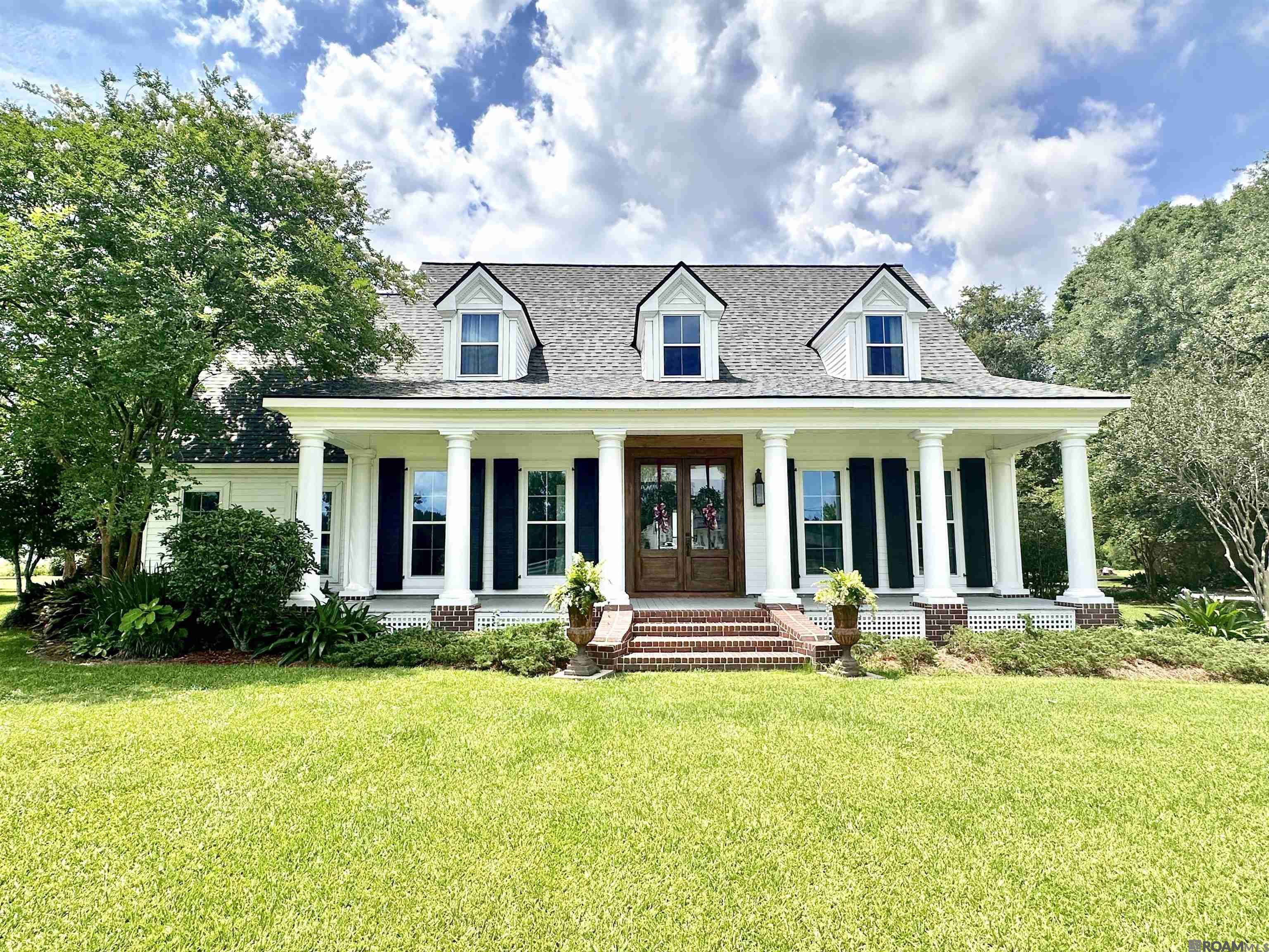 Stunning custom Southern home with a 2,500 sq ft workshop on 1.15 acres in the heart of Dutchtown! This well-maintained property sits on an industrial post-tension slab and offers space, charm, and flexibility—perfect for families or home-based businesses. Enjoy peaceful rural living with top-rated Dutchtown schools, shopping, and I-10 minutes away—and best of all, NO HOA. The home features a new roof, wood floors, updated windows, new front door, and fresh neutral paint. A classic Southern front porch with stately columns and mature landscaping creates great curb appeal. Inside, the 2-story foyer is flanked by a formal dining room and a private office with full bath and closet—easily a 5th bedroom. The spacious great room has cathedral ceilings, a wood-burning fireplace, and a wall of windows overlooking the backyard. The kitchen opens to a vaulted-ceiling breakfast area and includes granite counters, stainless appliances, and a unique 1918 antique cast iron sink. The downstairs primary suite offers a large ensuite bath and walk-in closets. Upstairs are 3 guest bedrooms (or use one as a large den) with all-new carpet. Outdoor living includes a new covered pavilion with 8-ft ceiling fan, brick courtyard, 4-tier fountain, covered back porch with ceiling fans, and a 20x25 storage/pump shed. The 50x50 workshop has two 14x14 roll-up doors, 20-ft sidewalls, a bathroom, and 1,000 sq ft storage loft—great for storage, workspace, or small business use. Located in Flood Zone X and never flooded. Two legally separated lots are available for purchase. This one-of-a-kind property blends Southern charm and modern convenience—schedule your showing today!