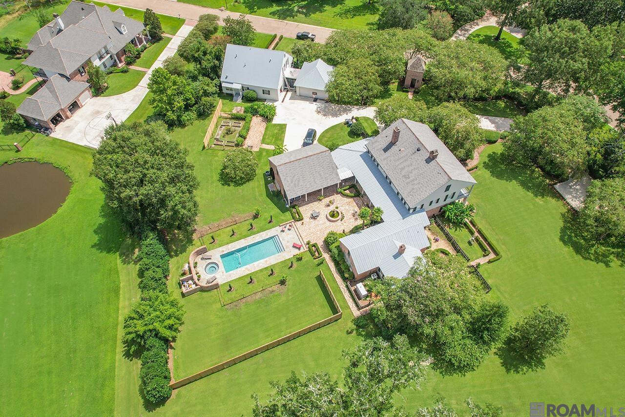 Located in the exclusive gated community of St. Andrews, just across the East Baton Rouge Parish line, this stunning 4-bedroom, 3.5-bath estate blends timeless elegance with modern convenience. Designed by renowned architect A. Hays Town and inspired by 1840s vintage architecture with Caribbean influences, the property has been featured in The Louisiana Homes of A. Hays Town and The Architectural Style of A. Hays Town and is listed with the Louisiana Historical Homes Foundation. Built in 1980, the main house sits on two picturesque acres with 250-year-old live oaks draped in moss, offering over 5,000 square feet of living space. Features include 200 year old heart pine floors, soft red brick sourced from a New Orleans convent dating back to 1840, a grand foyer, cypress ceilings, large beams, and a handcrafted cypress mantle framing the wood-burning fireplace. French doors and large windows flood the living areas with natural light and open to a covered porch, brick patio, hot tub, and pool. The kitchen and breakfast area maintain the home’s historic charm with a plank wood ceiling, and exposed beams and an additional wood-burning fireplace adds warmth to the space. The primary suite features its own fireplace, an office with exterior access, and a spacious walk-in closet. Upstairs are three more bedrooms and two full baths, while a separate studio above the garage serves as a guest suite, game room, or private space. A 2,300-square-foot guest cottage, scripted by A. Hays Town as well offers two bedrooms, a bonus room, a full kitchen, a living area, and a double garage by Andy McDonald adds to the appeal.  Adding to the charm, a beautifully designed pigeonnier by Al Jones serves as a private chapel. The estate also includes a whole-home Generac generator. This exceptional property blends historic elegance with modern comforts, offering a rare opportunity to own a piece of Louisiana history.