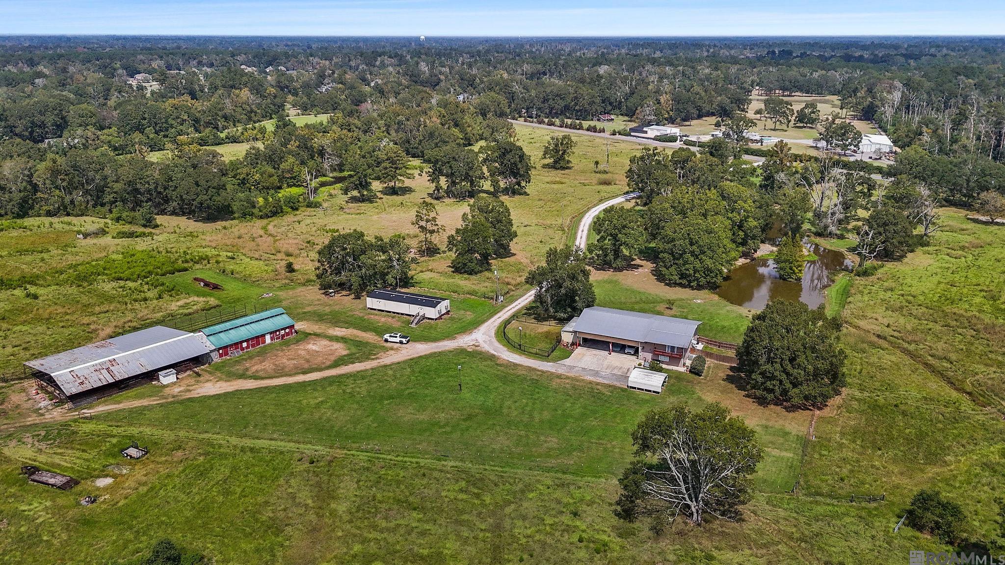 Unlock the potential of this remarkable 113.09-acre property, offering the perfect combination of rural charm and unmatched opportunity. Currently zoned R-1, this land is primed for development, whether you envision a family estate, a residential community, or another project to make the most of its vast space. At the heart of the property sits a 2,250 sq ft metal structure home, providing immediate comfort while you plan for the future. The open floor plan creates a welcoming atmosphere, with a spacious main level that includes a large bedroom, a full bathroom, and a bright kitchen with modern finishes. Stainless steel appliances and granite countertops elevate the kitchen, which flows seamlessly into the living and dining areas—perfect for both relaxing and entertaining. Upstairs, a cozy loft bedroom offers a quiet getaway, complete with a private balcony to enjoy sweeping views of the land.  Outside, the property extends its appeal with a large covered carport and patio area, ideal for outdoor living or hosting gatherings. The surrounding landscape features three tranquil ponds and expansive pastures, accented by scattered wooded areas that add natural beauty and privacy. An outdoor kitchen and a substantial storage building provide additional amenities to enhance your lifestyle.  The property is fully fenced and cross-fenced, making it an excellent choice for agricultural use or livestock management. A large, well-equipped barn serves as both a workspace and storage area, offering convenience for any farming or ranching activities.  In addition to its agricultural appeal, this land offers a variety of recreational opportunities. The property’s diverse terrain and abundant wildlife make it a haven for outdoor enthusiasts.  Located just south of Denham Springs, this property blends the peace of country living with the promise of future growth and limitless possibilities.
