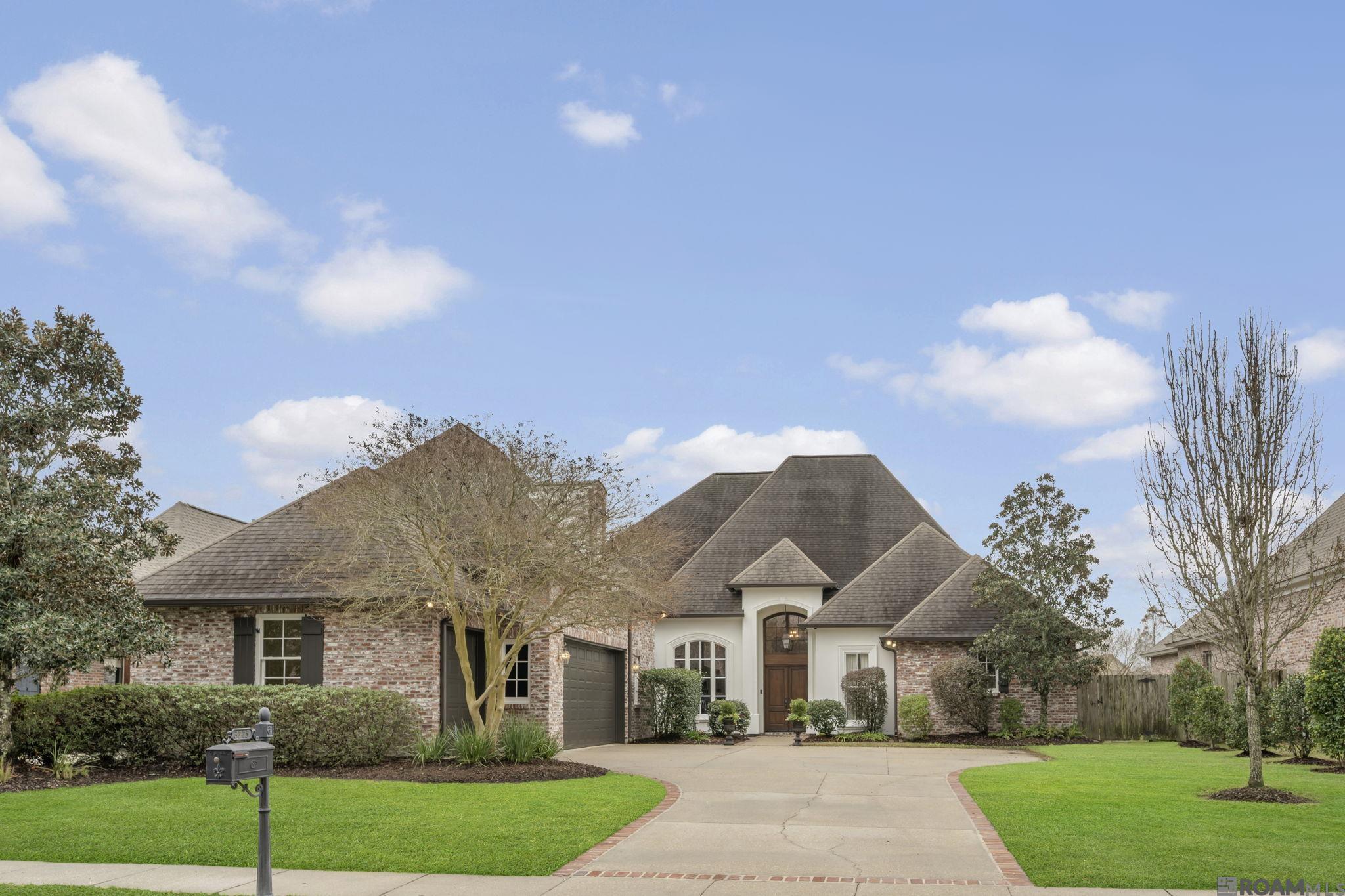 What a view! This stunning lakefront home with a custom saltwater pool is nestled in sought-after Lexington Estates, just minutes from LSU. From the moment you step inside, you’re greeted by breathtaking panoramic lake views that set the tone for this exceptional property. The sun-filled living room showcases soaring 12-foot ceilings, triple crown molding, classic built-ins, and an elegant marble gas fireplace—perfectly blending comfort and sophistication. Designed for both everyday living and entertaining, the gourmet chef’s kitchen is a showstopper, featuring a 6-burner gas range with variable heat levels, KitchenAid appliances, silent dishwasher, ice maker, pot filler, custom cabinetry with spice drawers, abundant storage, and an oversized island topped with exquisite granite countertops. At the heart of the home, a stylish wet bar offers custom glassware storage, an undermount sink, and a wine refrigerator—ideal for hosting and entertaining with ease. The spacious primary suite is a private retreat with tranquil lake views and a luxurious spa-inspired bath complete with custom built-ins, soaking tub, and a stunning multi-head shower with rain feature. This well-appointed home offers five bedrooms plus a dedicated office with built-ins, perfect for students or professionals working from home. Upstairs, you’ll find a large private bedroom with a full bath—ideal for guests. Additional highlights include an oversized laundry room with sink, storage, and ironing board (washer and dryer included). The two-car garage provides extra storage along with a versatile third bay, perfect for a workshop, compact vehicle, or recreational equipment. Step outside to an entertainer’s dream: an expansive outdoor living area with a full kitchen (gas grill, refrigerator, sink), oversized fireplace, and a resort-style backyard. Unwind by the sparkling saltwater pool, enhanced by a soothing waterfall feature, and take in the peaceful lakefront setting. Luxury, Lifestyle, Location!